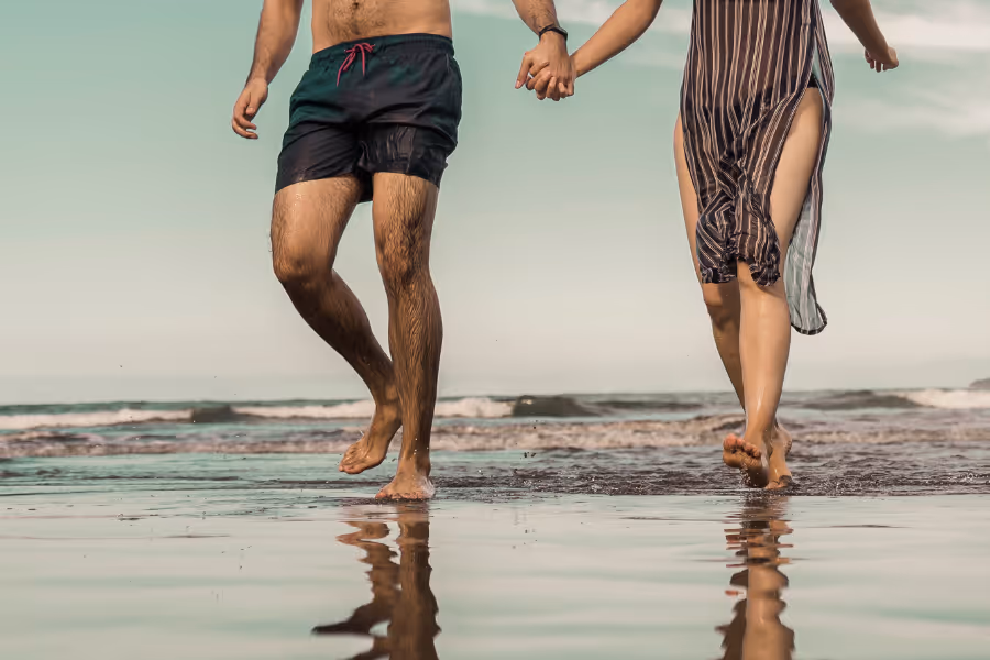 Un couple se promène heureux sur la plage, libéré de la douleur d'un kyste pilonidal.