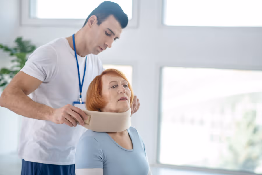 Un patient âgé ayant subi une laminectomie cervicale se fait poser une minerve par un kinésithérapeute.