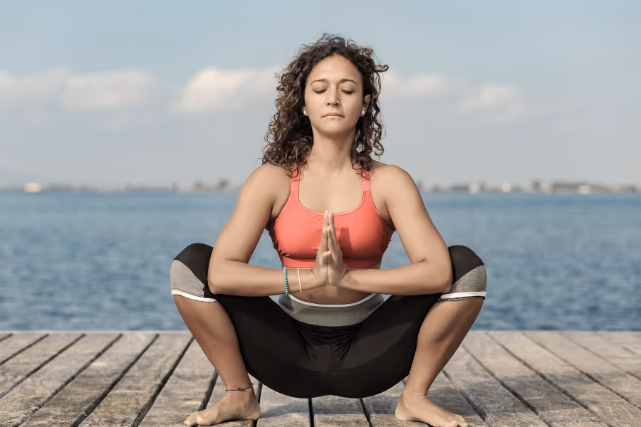 Woman on a dock performing deep squat yoga pose