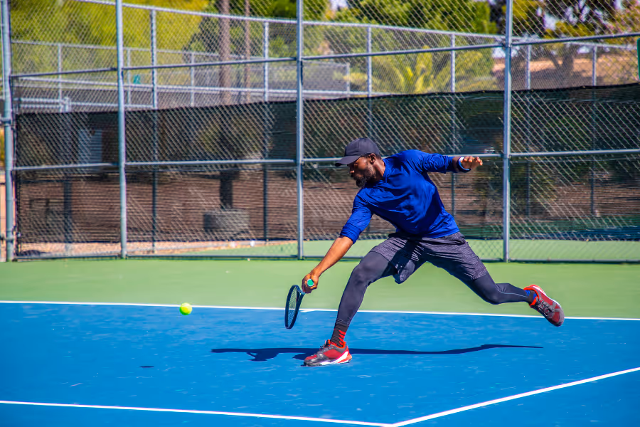 Man playing tennis in tight blue clothing, pivoting for the ball