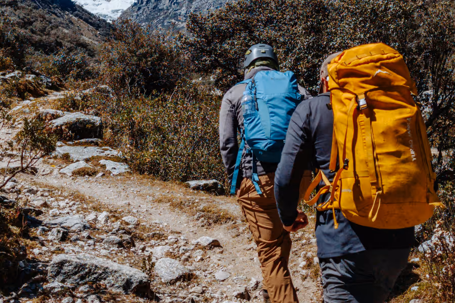 Two hikers with backpacks walking up a steep, uneven hiking trail