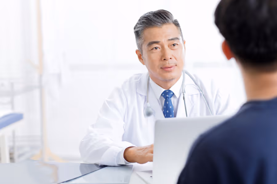 Male surgeon speaking with patient in lit office, concerned about buttock pain