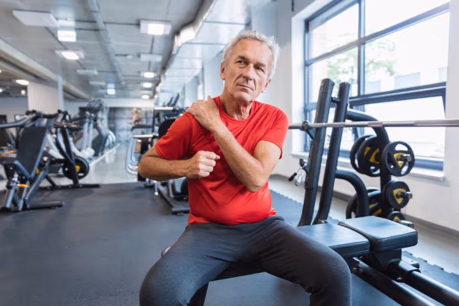 Older male patient on a bench press, holding shoulder