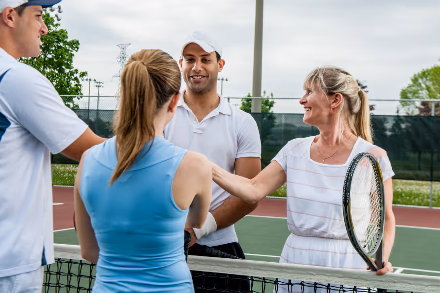 Two doubles teams in tennis shaking hands at the net