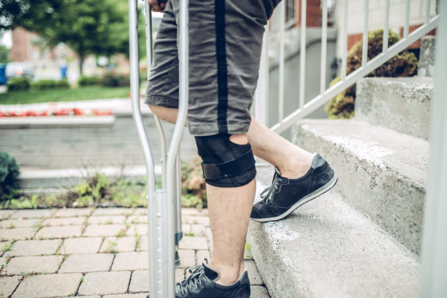 Closeup of man's knee, walking downstairs assisted by crutches after ACL surgery