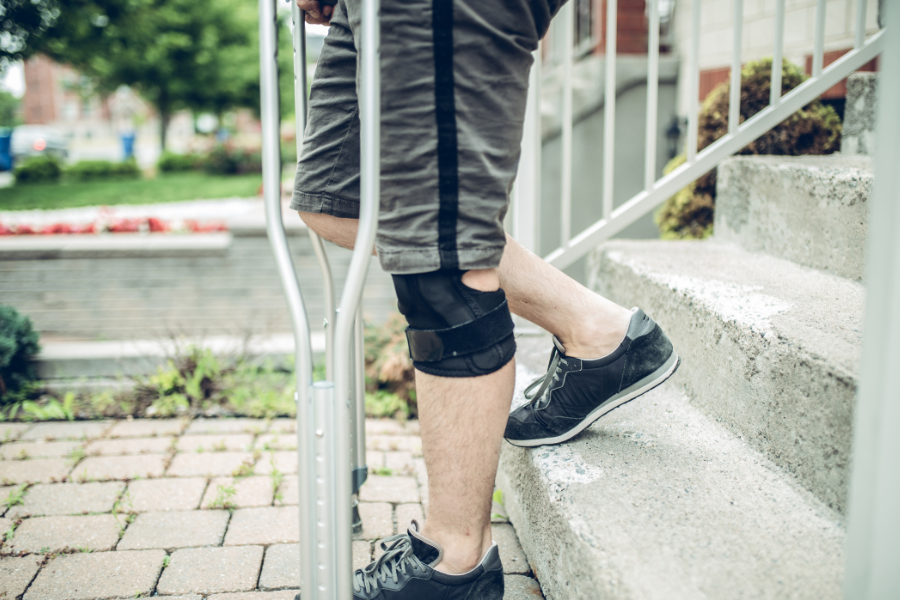 Closeup of man's knee, walking downstairs assisted by crutches after ACL surgery