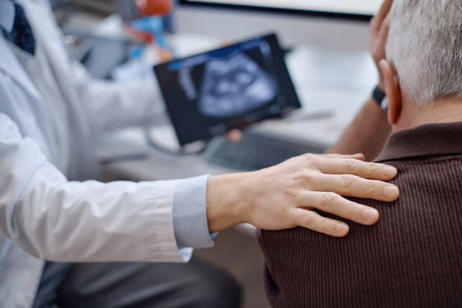 Urologist consoling older male patient, visible enlarged prostate shown on ipad