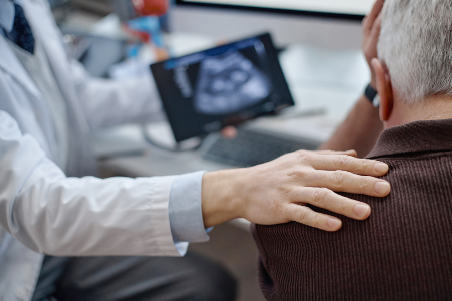 Urologist consoling older male patient, visible enlarged prostate shown on ipad