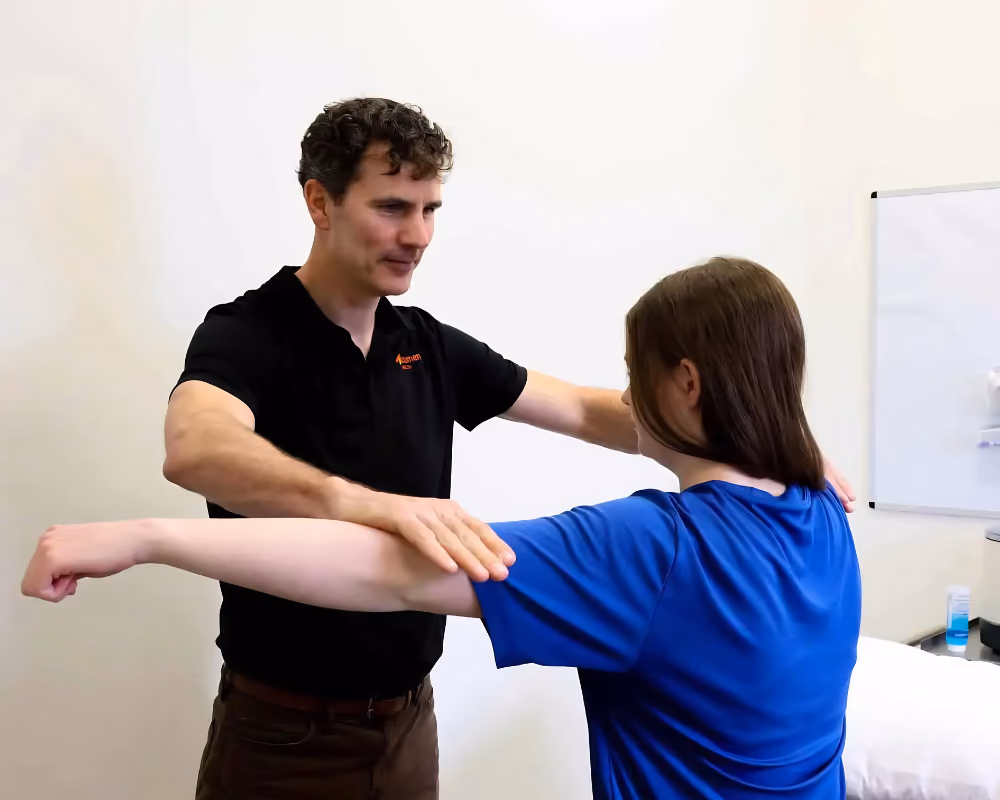 Dr Myden testing female patient's shoulder mobility in clinical setting.