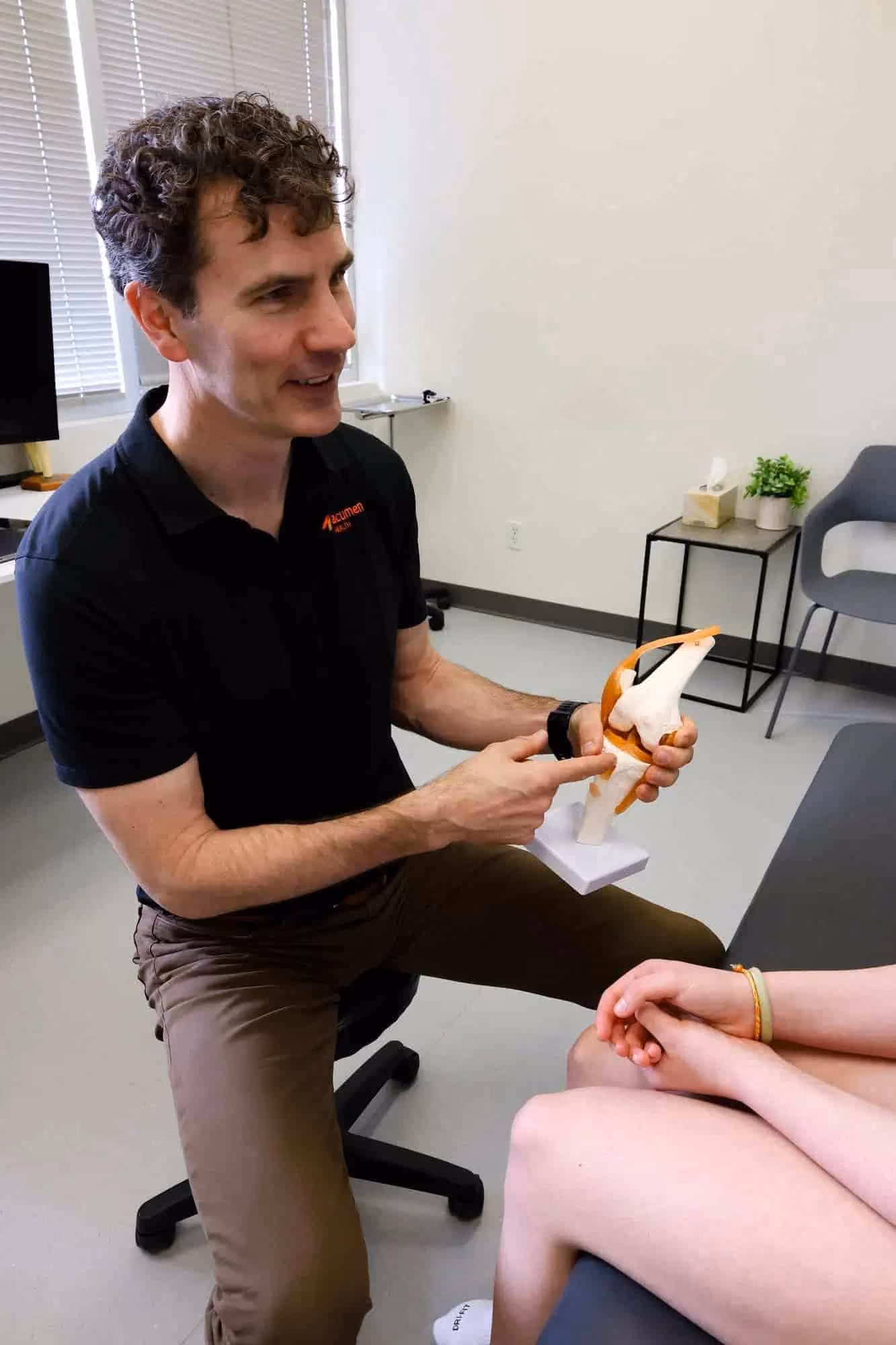 Dr Myden using a diagram to show patient knee joint during a consultation in clinical setting.