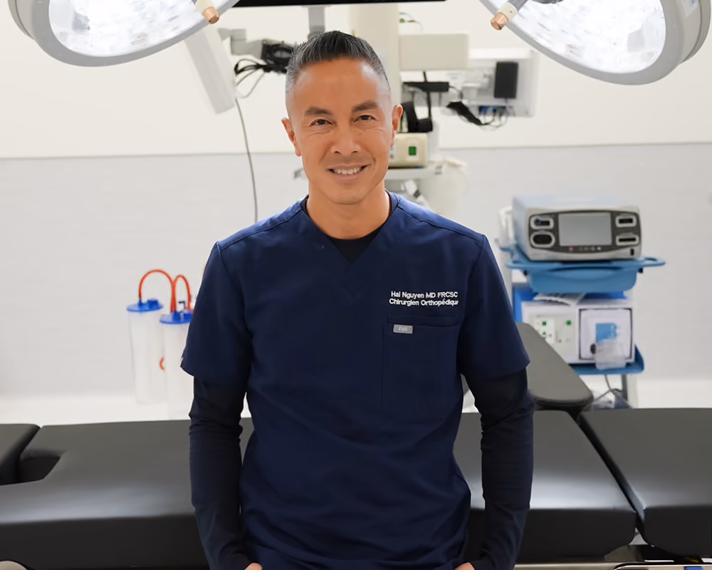 Le Dr Hai Nguyen est assis sur une table d'opération dans un environnement clinique propre.