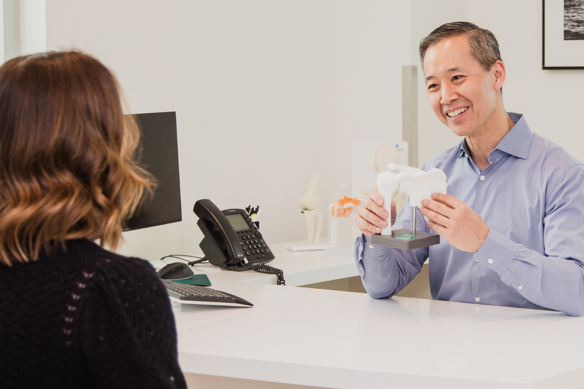 Dr. Lo showing a female patient a diagram of the shoulder joint in clinical setting.