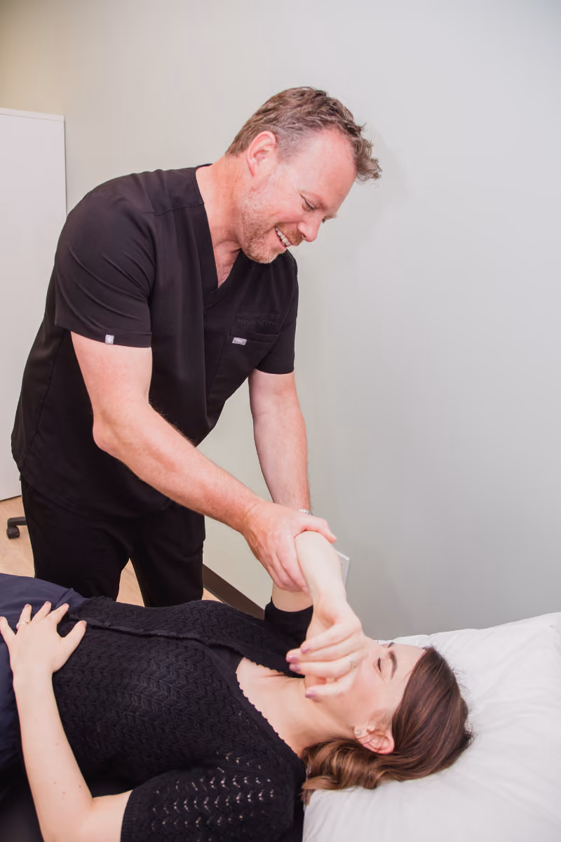 Dr. Leblanc working with female patient to assess shoulder on a physio table.