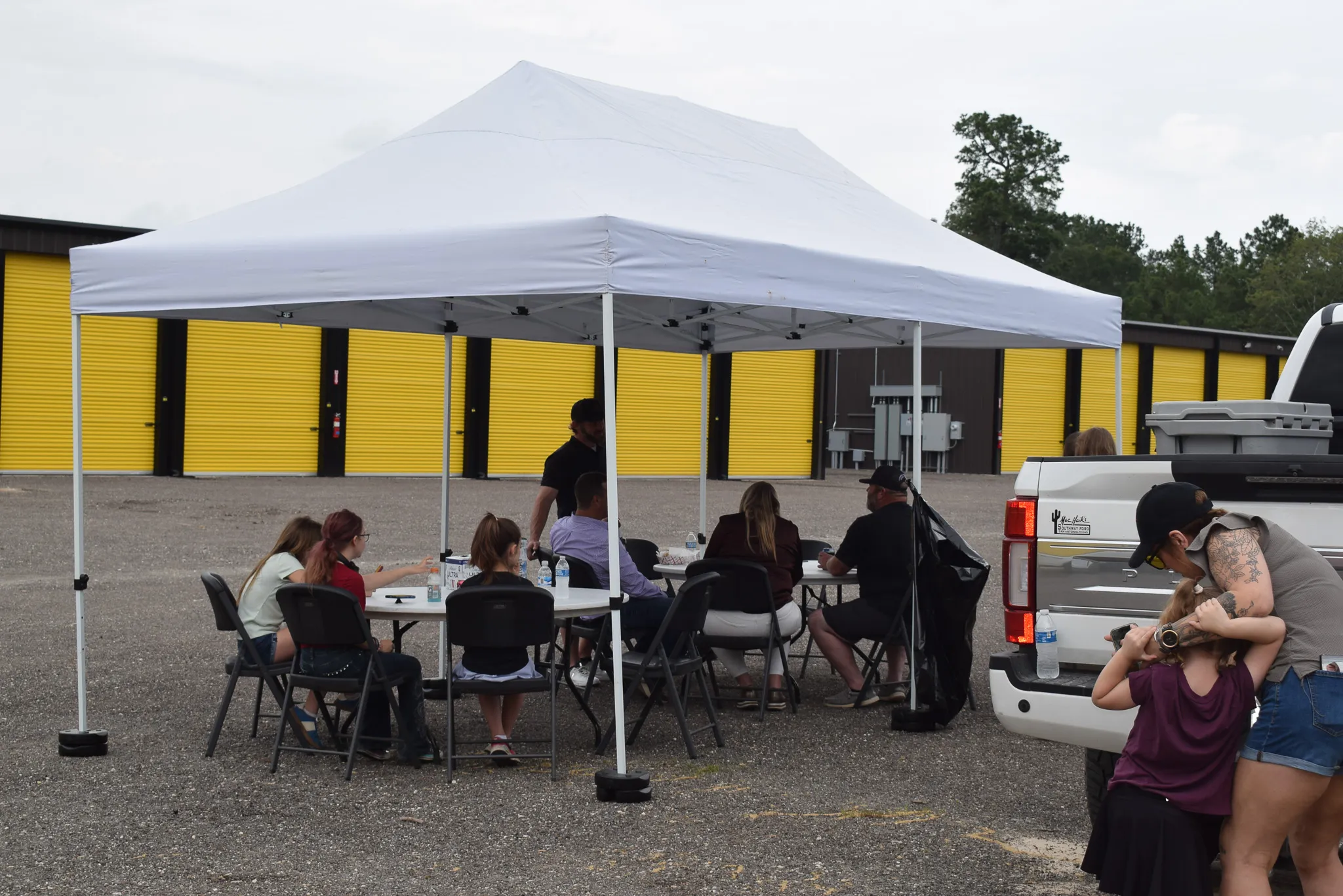 A white event canopy set up in front of the yellow storage unit doors at the Foxgate Boat & RV Storage grand opening.