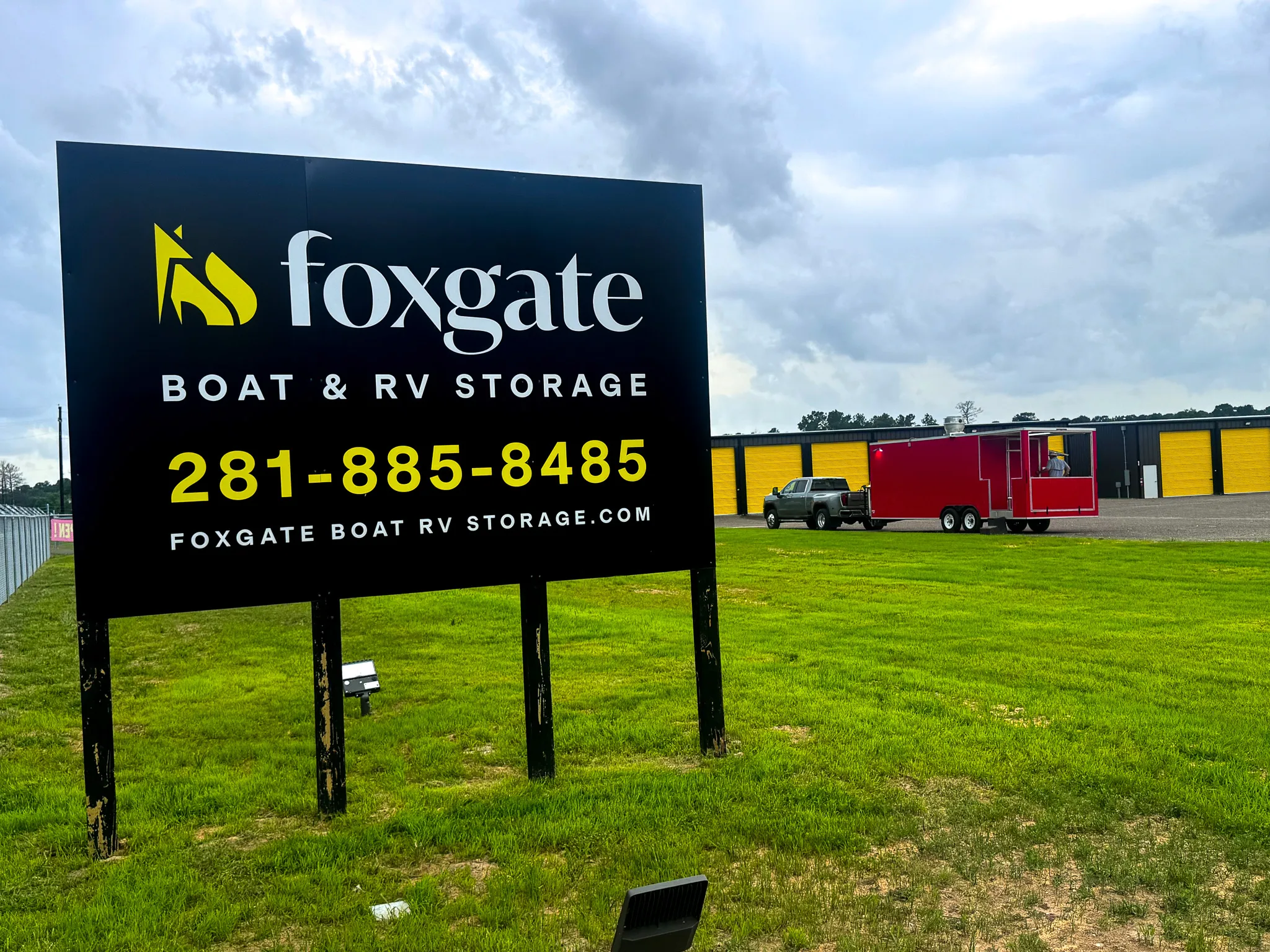 Foxgate Boat & RV Storage entrance sign with the company logo and phone number, in front of the storage buildings with yellow doors.