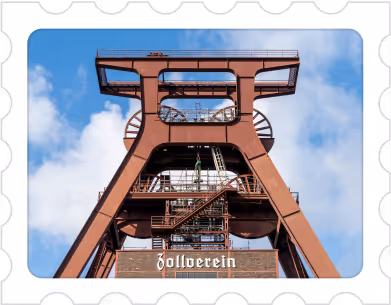 Rust-colored industrial mining tower structure against a blue sky with clouds, labeled 'Zollverein'.