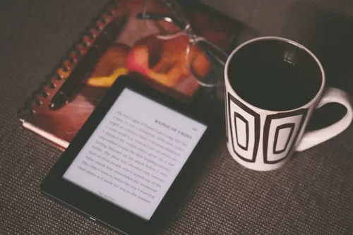 Kindle e-reader with a coffee mug, with a note taking book in the surrounding.
