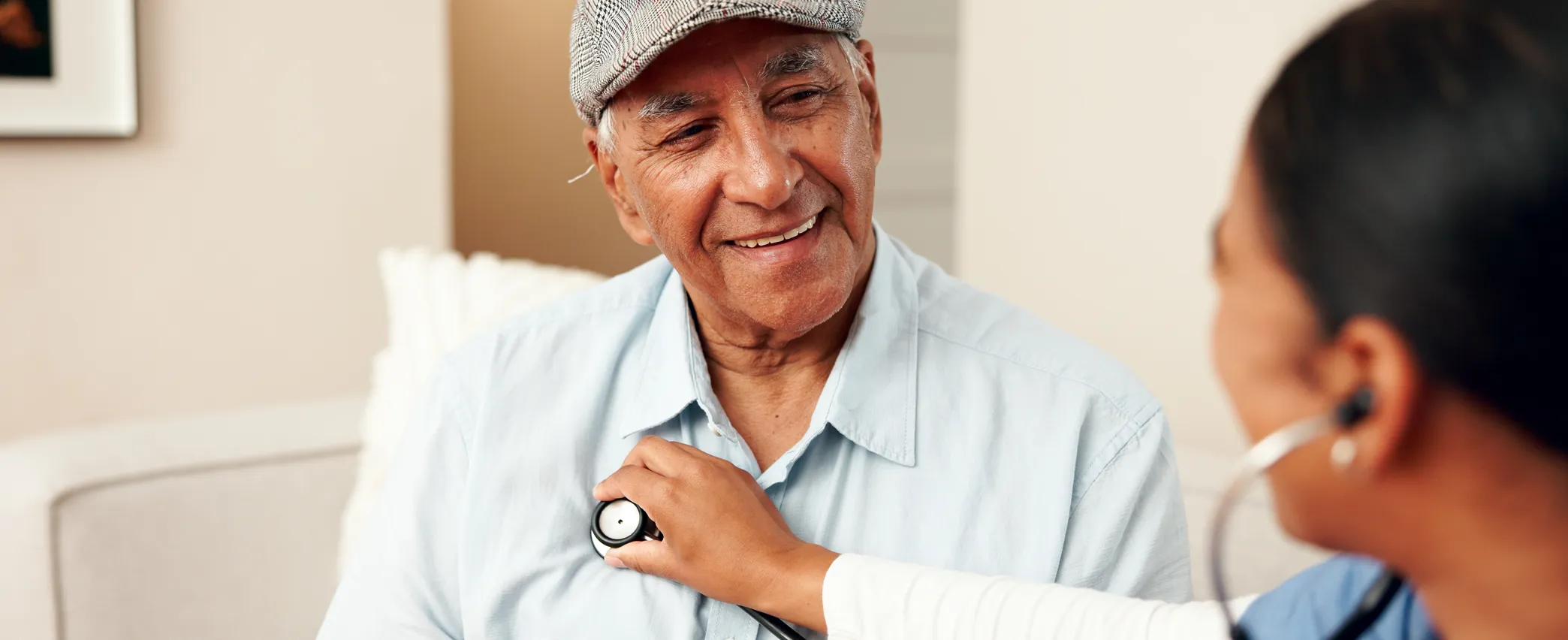 Smiling elderly man wearing a cap having his heartbeat checked with a stethoscope by a healthcare professional.