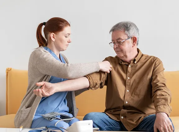 Nurse measuring blood pressure of elderly man sitting on a yellow couch.