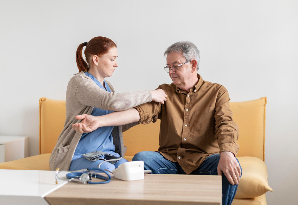 Nurse measuring blood pressure of an elderly man sitting on a yellow couch.