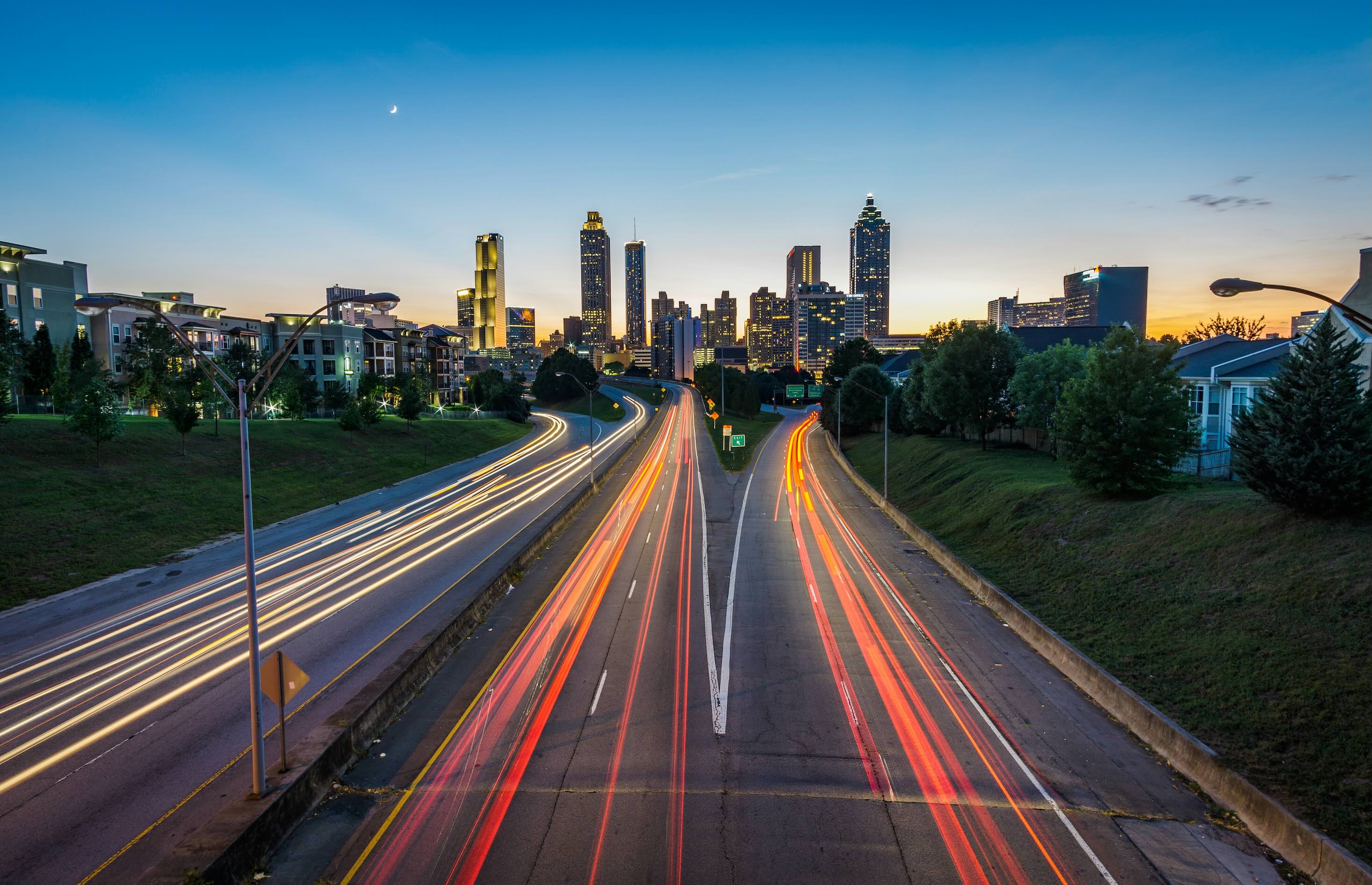 Downtown Atlanta skyline at dusk with light trails from cars on a busy highway leading into the city.