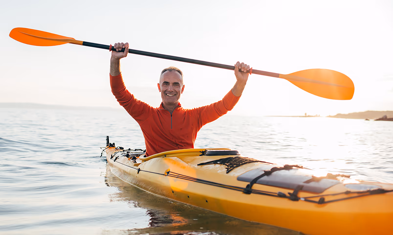 Smiling senior man in kayak holds paddles high