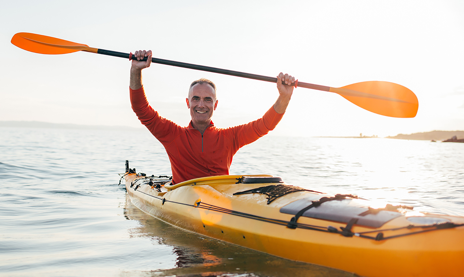 Smiling senior man in kayak holds paddles high