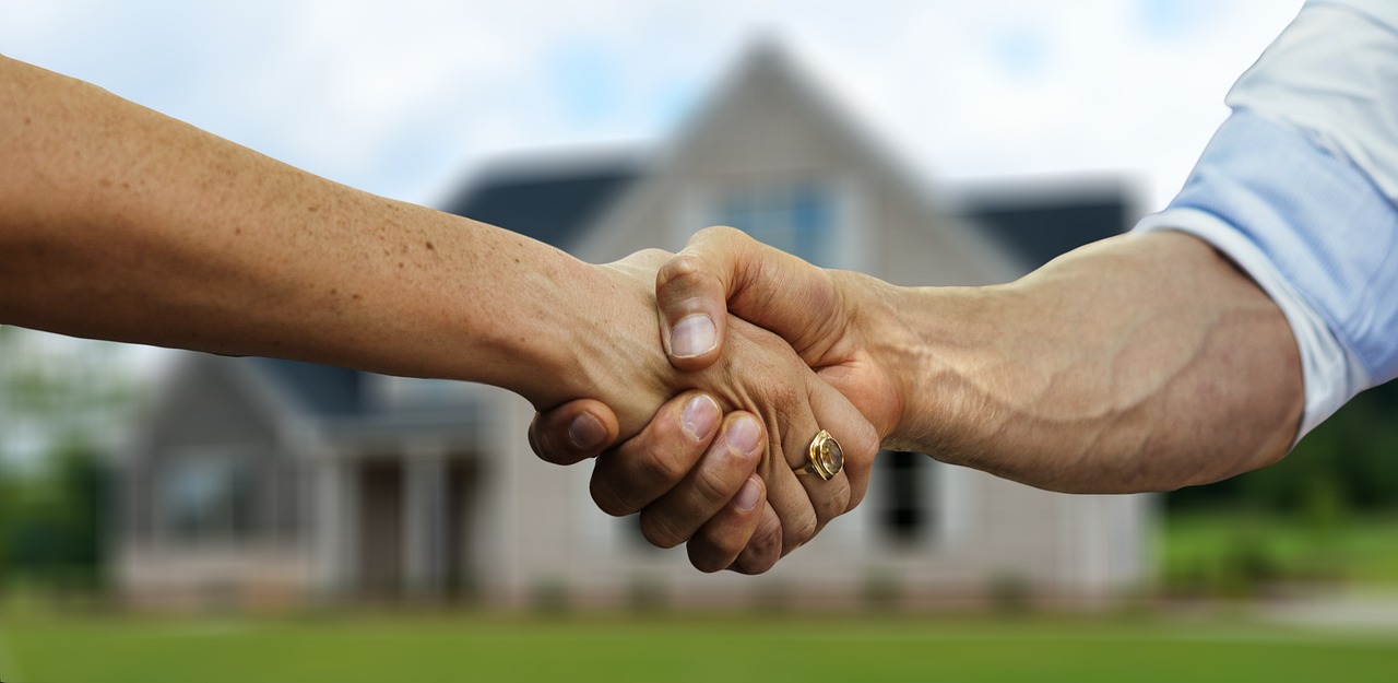Two people shake hands in front of a house, symbolizing a real estate deal or agreement.