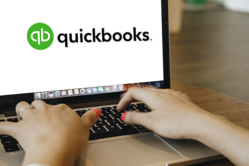 Hands typing on a laptop displaying the QuickBooks logo on the screen.