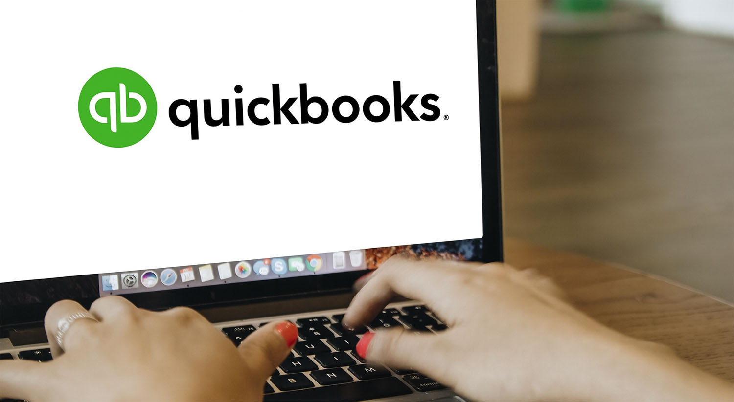 Hands typing on a laptop displaying the QuickBooks logo on the screen.