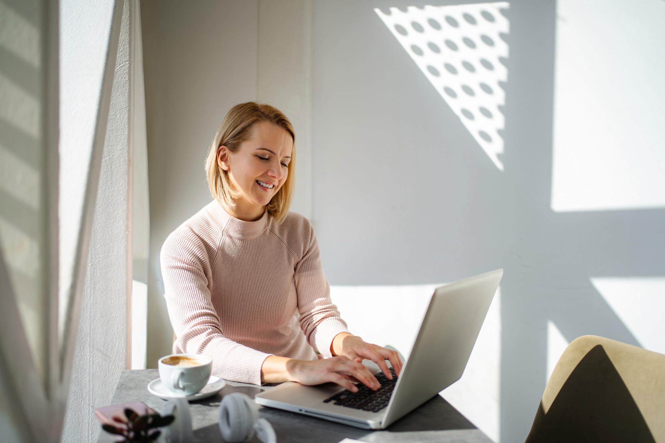 Person working on a laptop at a table with coffee and headphones nearby.