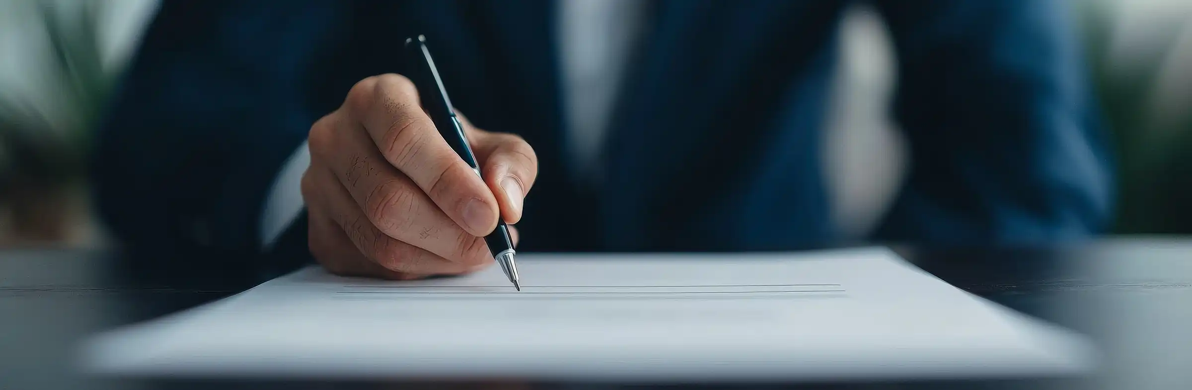 Smiling bald man in a blue shirt and checkered tie sitting at a wooden table working on a laptop with a Batman-themed mug nearby.