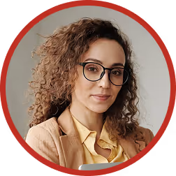 Portrait of a woman with curly hair, glasses, and a beige blazer over a yellow blouse, smiling slightly against a neutral background.