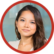 Portrait of a young woman with long dark hair wearing a white top, smiling softly against a blurred indoor background.