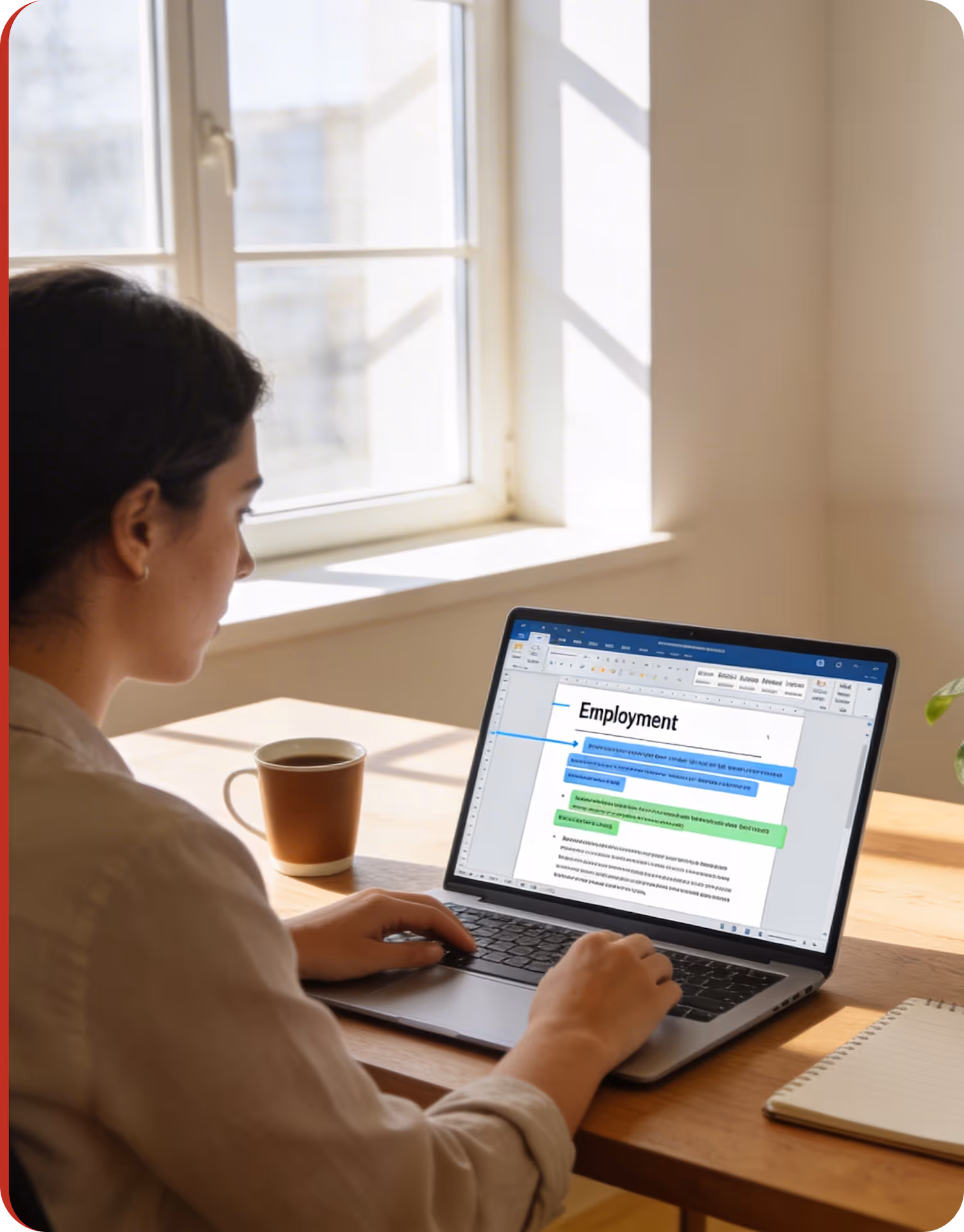 Person working on a laptop with a document titled 'Employment' open on the screen, sitting by a sunlit window with a coffee mug and notebook on the table.