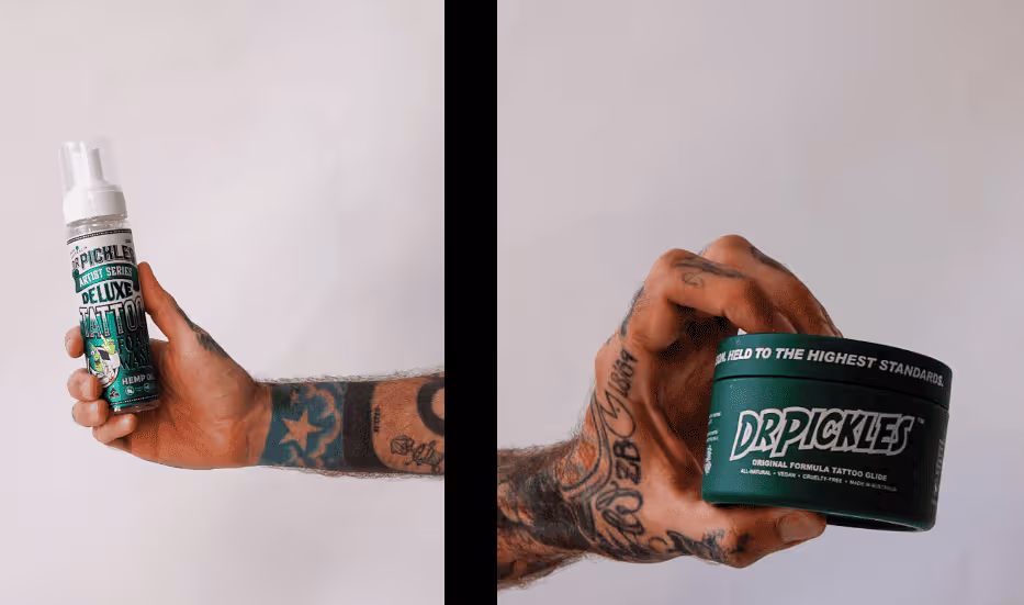 Tattooed arm holding two Dr. Pickles tattoo care products: a bottle of Deluxe Tattoo Aftercare and a jar of Original Formula Tattoo Glide.
