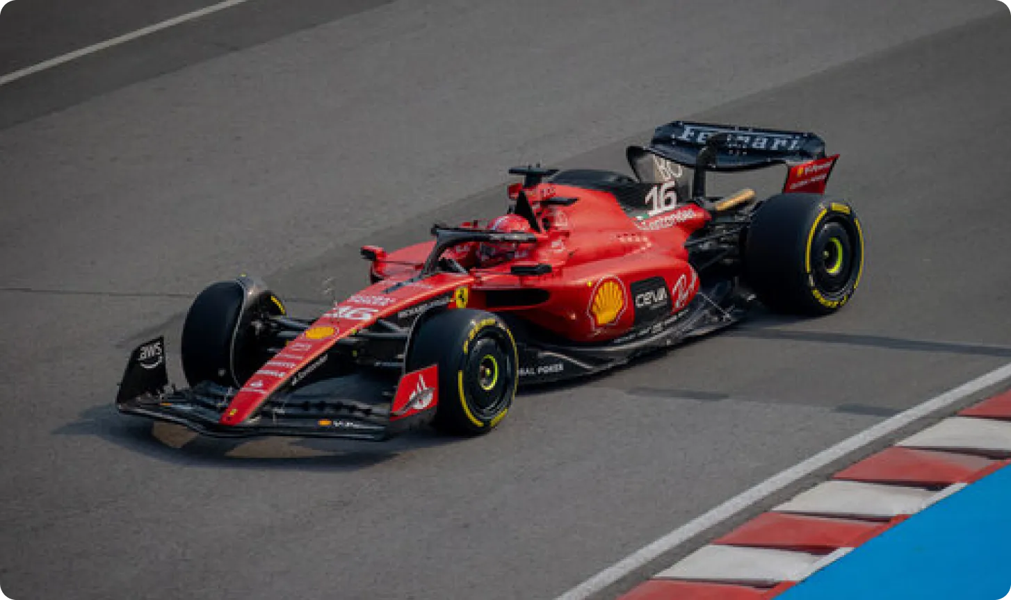 Red Ferrari Formula 1 race car number 16 driving on a racetrack near red and white striped curbs.