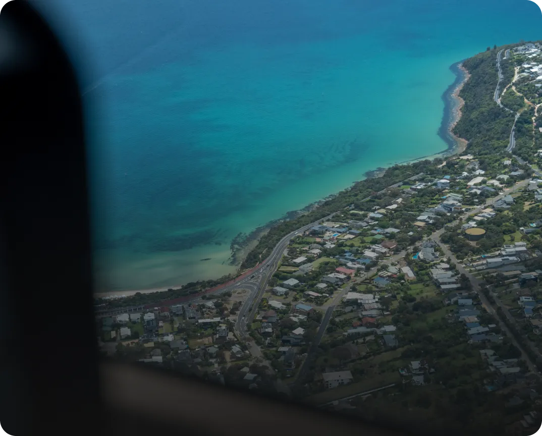 Aerial view of a coastal town with turquoise ocean water and a winding road along the shoreline.