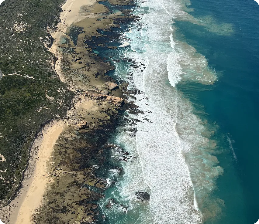 Aerial view of a rugged coastline with sandy beaches, rocky shorelines, and waves crashing into the shore.