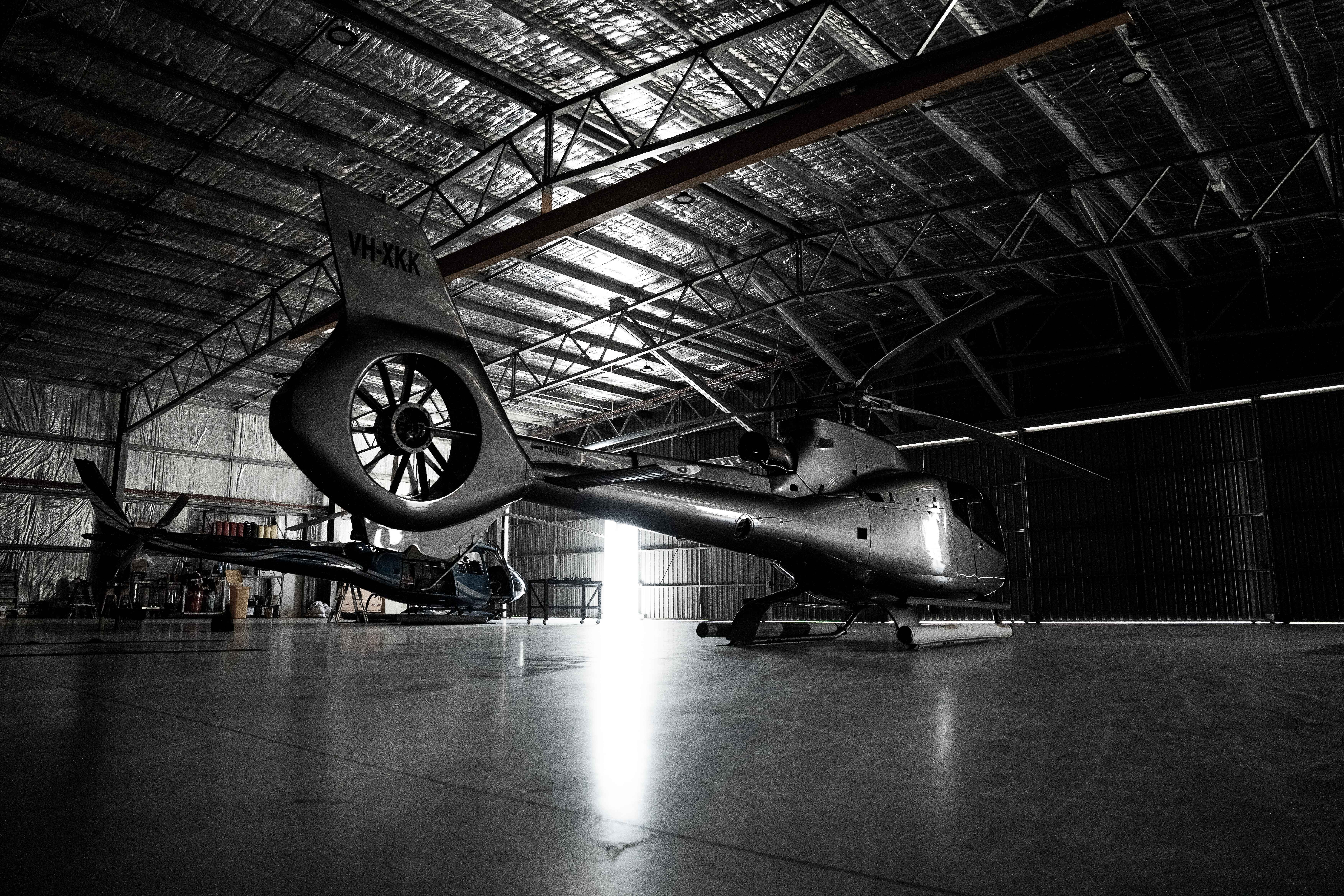 Two helicopters parked inside a dimly lit hangar with light streaming through an open door in the background.