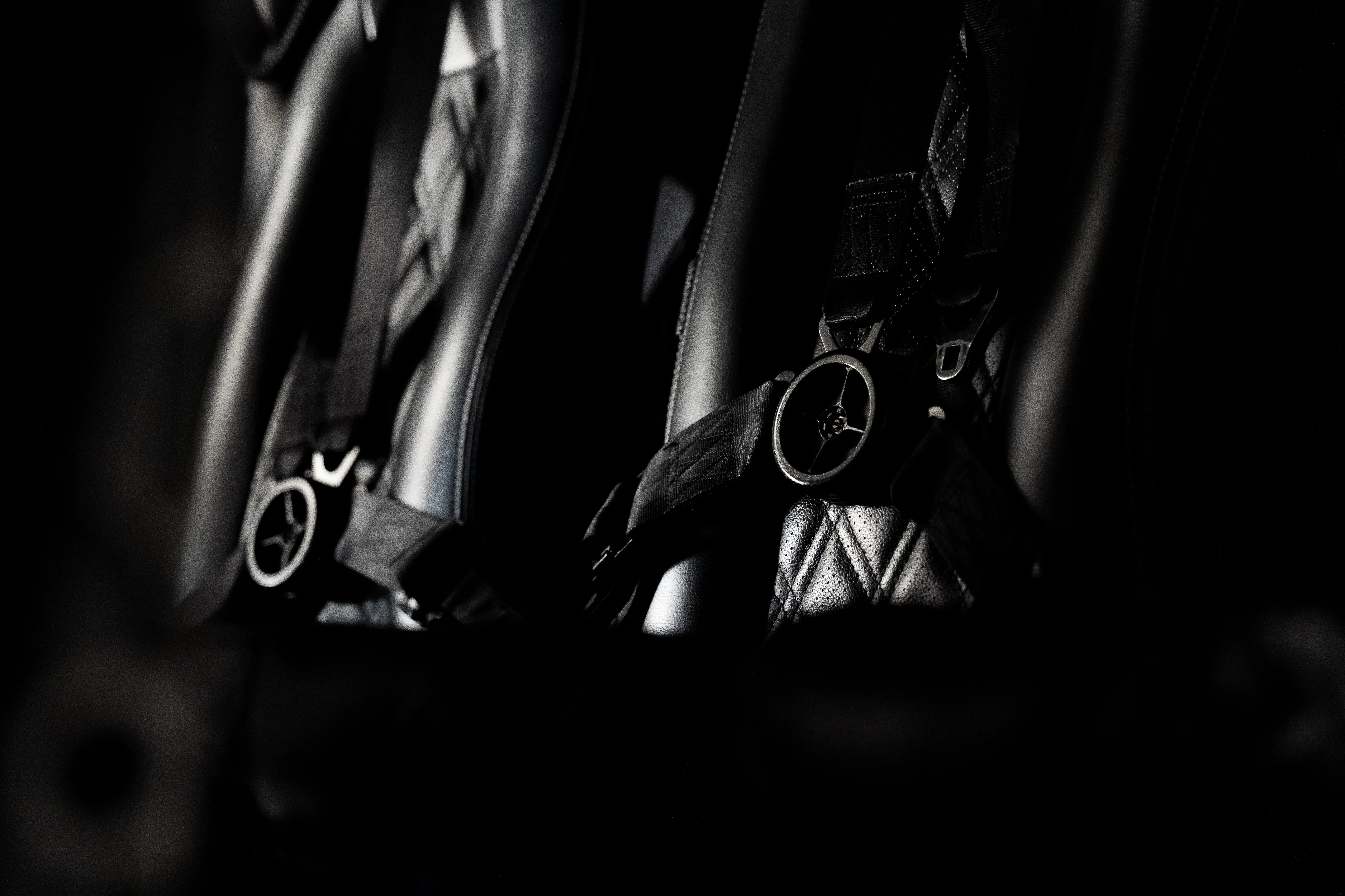 Close-up of dark leather seats with safety harness buckles in a dimly lit environment.