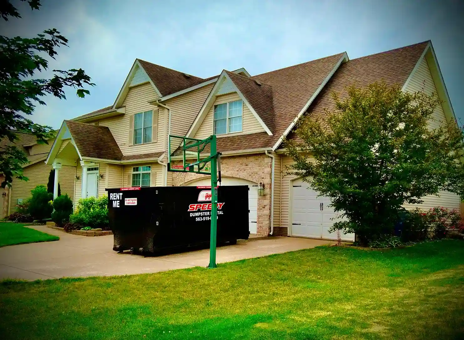 Large dumpster in driveway of suburban two-story house with green lawn