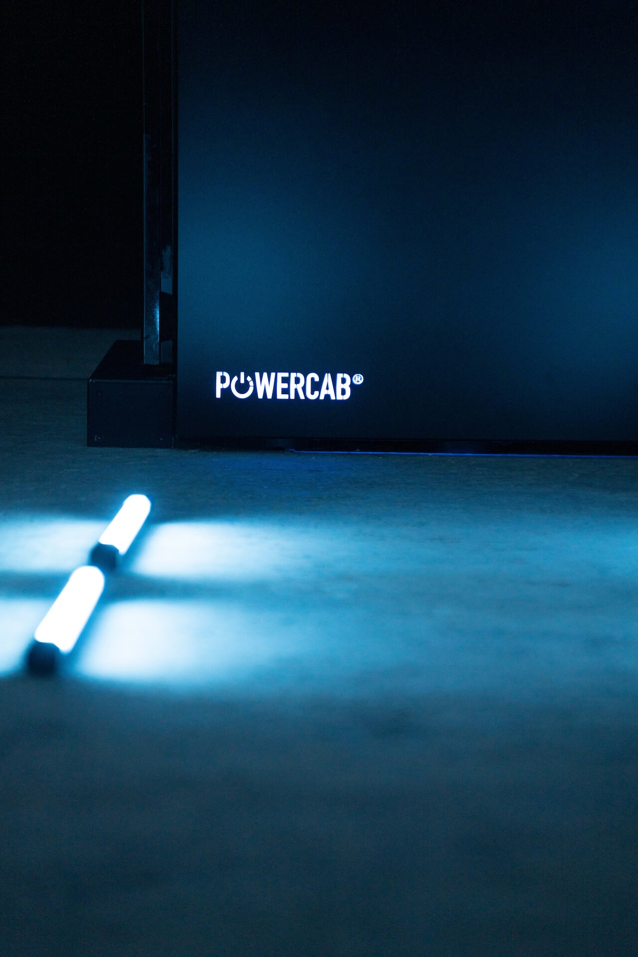 Nahaufnahme der unteren Ecke eines Geräts mit der Aufschrift ‚POWER CAB‘ und zwei leuchtenden weißen Stäben auf einem dunklen Boden.