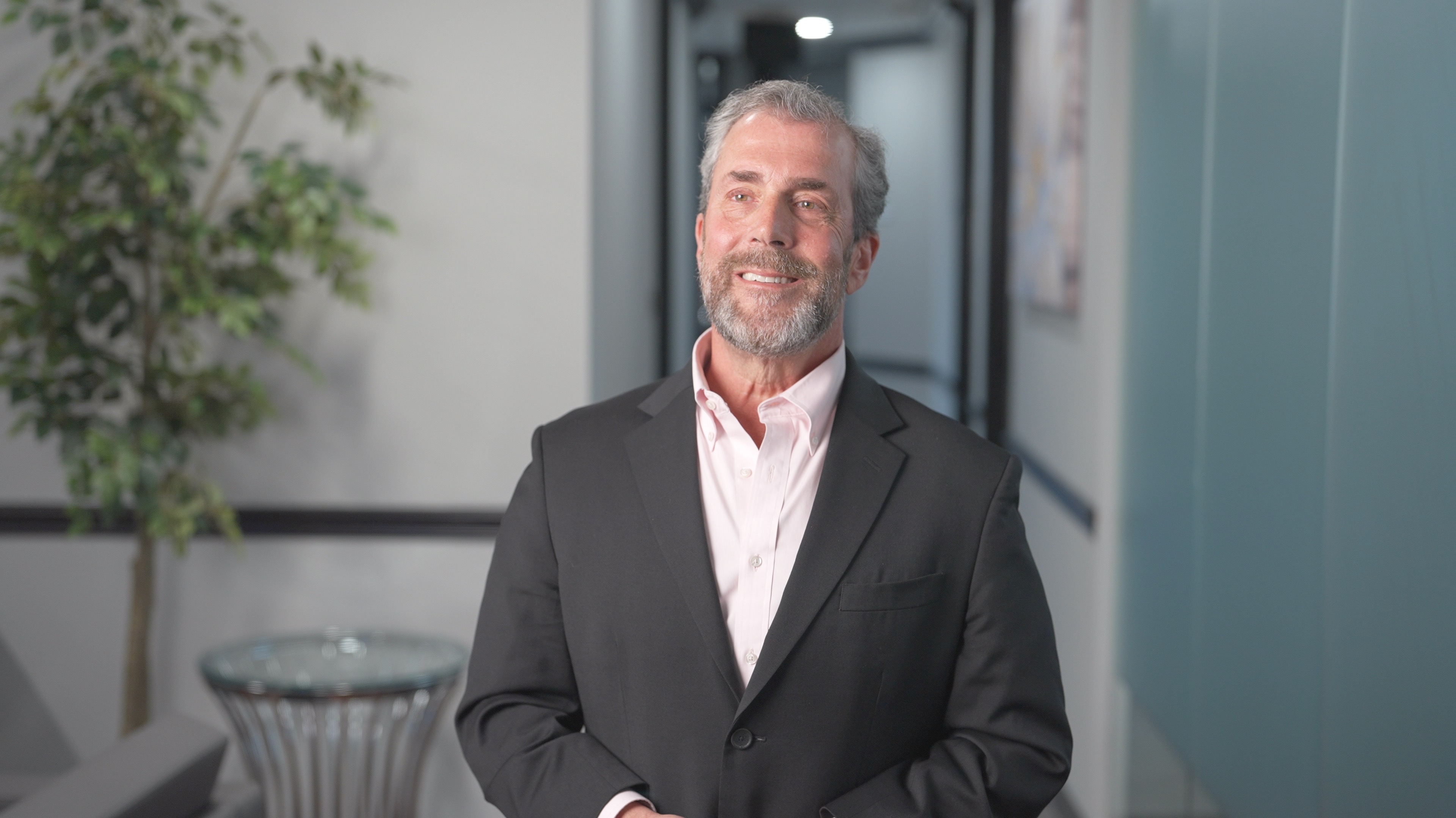 Smiling CIO from New Day wearing a black blazer and light pink shirt in an office hallway.
