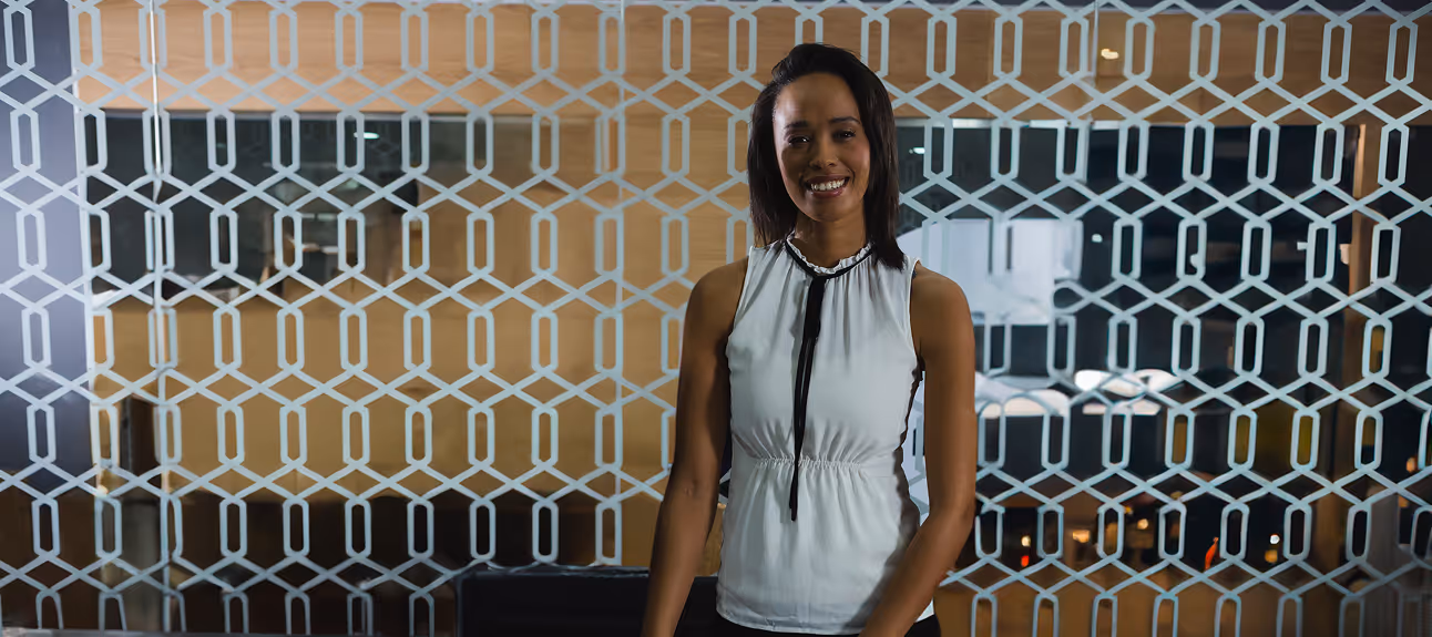 Professional woman standing in a modern office, smiling confidently before a wellness meeting.