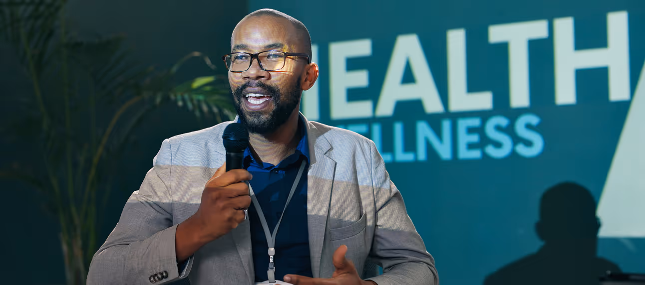 Male speaker presenting at a health and wellness event with HealthFusion branding in the background.