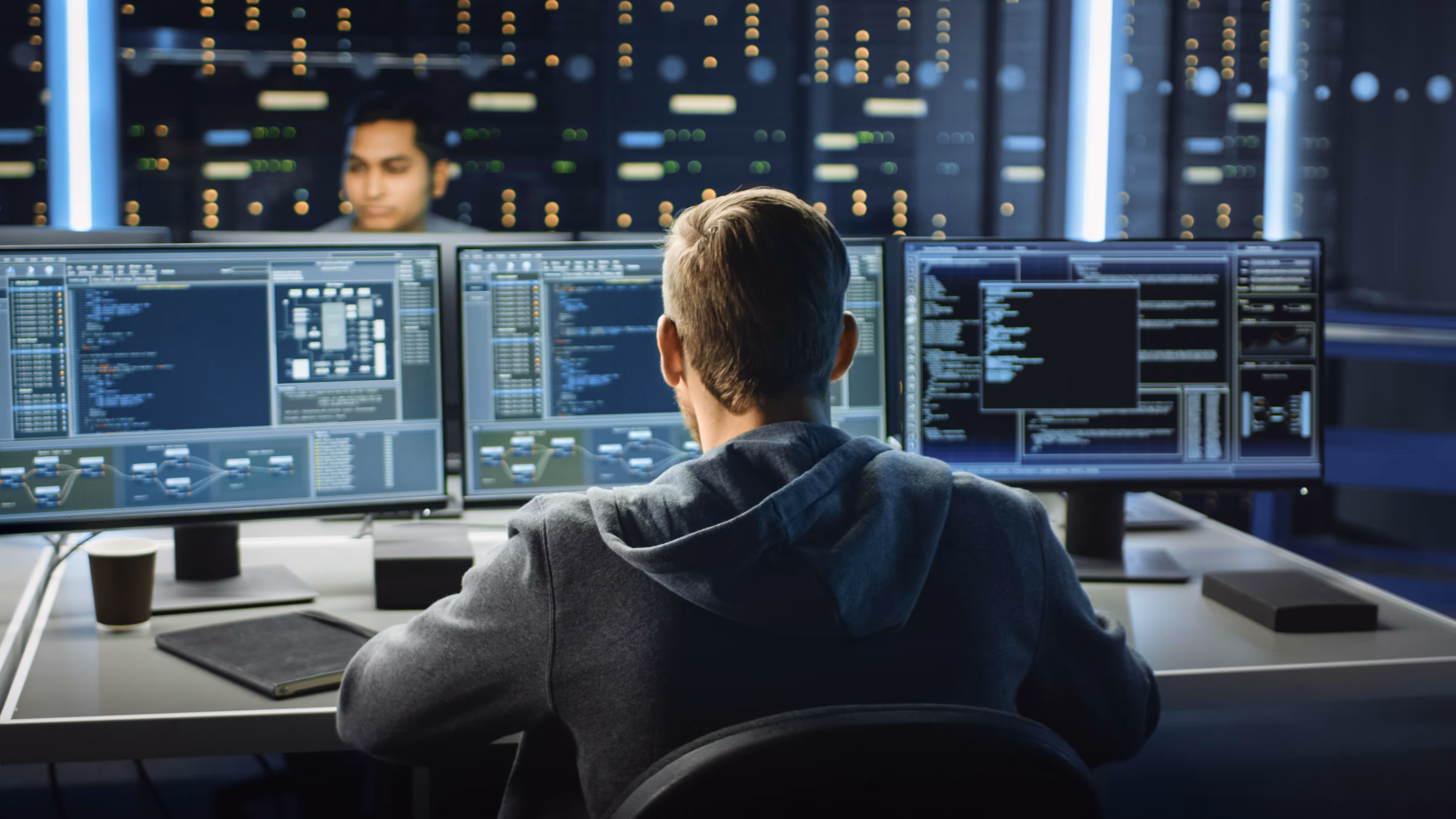 man sitting in front of 3 monitors working