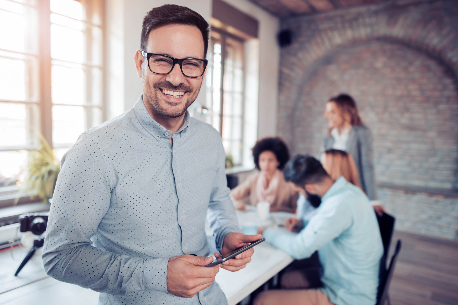 Portrait of a smiling man with glasses in an office holding a phone