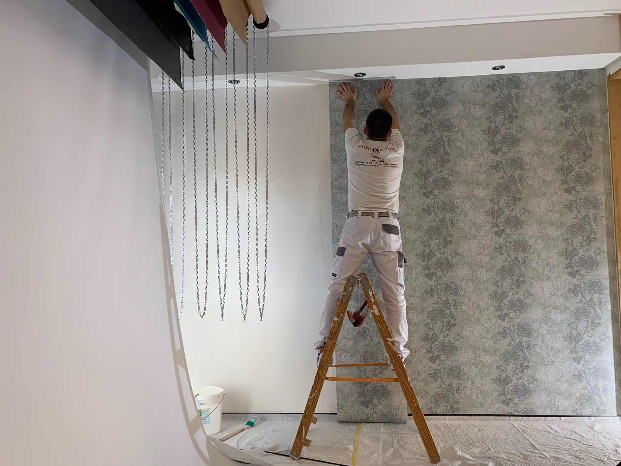 Maler auf Leiter, der eine gemusterte Tapete an die Wand klebt.