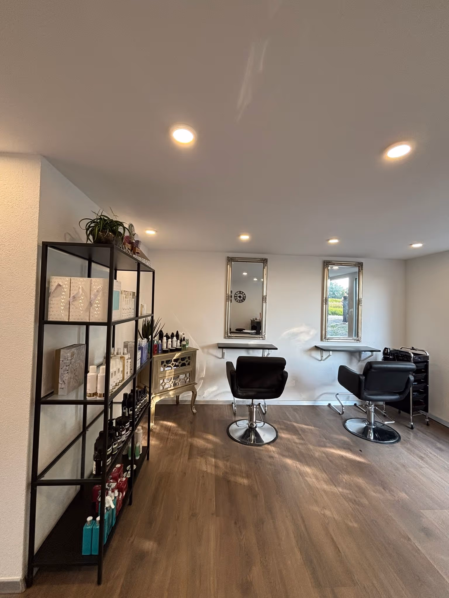 Moderner Friseursalon mit zwei schwarzen Friseurstühlen vor Spiegeln und Regalen mit Haarpflegeprodukten.